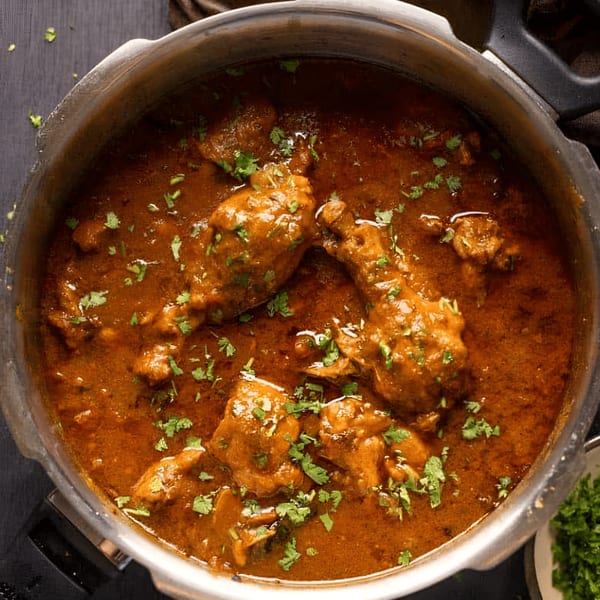 Overhead view of a large pot filled with rich, brown Indian chicken curry, garnished with fresh cilantro.