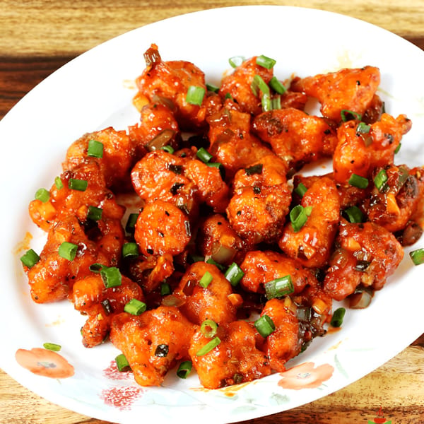 Virasat Indian Cuisine's Gobi Manchurian, a vibrant orange-red dish with green onion garnish on a white plate.