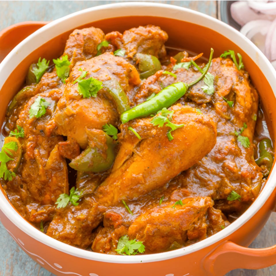 Virasat Indian Cuisine's chicken curry with green peppers, cilantro, and a chili in an orange bowl.