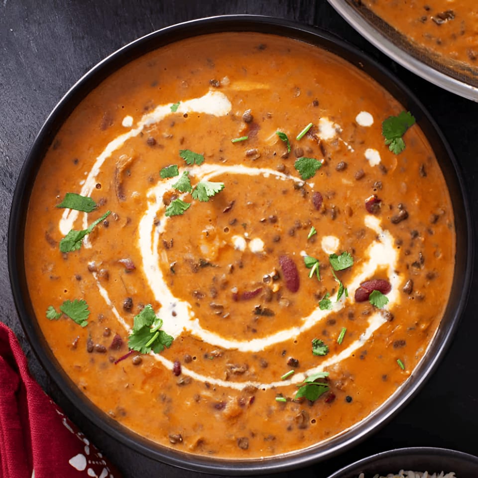 Close-up of a bowl of creamy orange Indian Dal Makhani, garnished with cilantro and cream swirls.